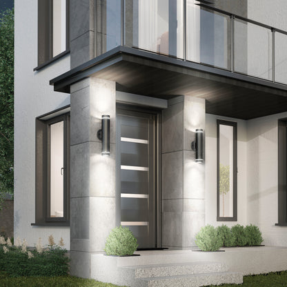 A modern house entrance features a sleek gray front door with horizontal glass panels, concrete steps, small green shrubs, and C7 Pro Outdoor LED Wall Lights on either side of the entryway.