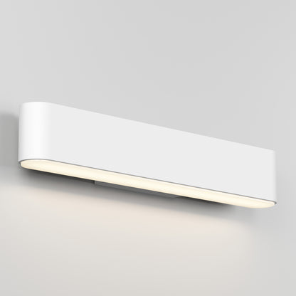 The Willow LED Vanity 3CCT Light features a modern rectangular design with rounded edges, emitting a soft, warm glow from beneath to elegantly illuminate any space when mounted on a light gray wall.