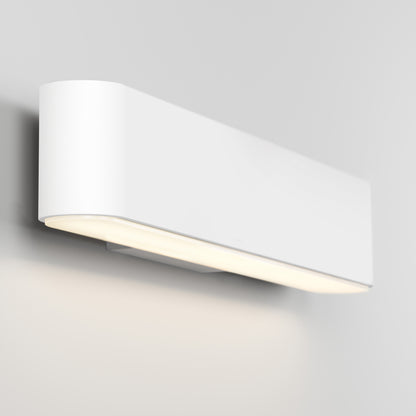 The Willow LED Vanity 3CCT Light, with its modern rectangular rounded-edge design, is mounted on a light gray wall; it emits soft downward lighting and offers adjustable color temperature for versatile illumination.