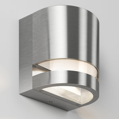 The Valor Round LED Indoor/Outdoor Wall Light features a modern curved cylindrical design in brushed stainless steel with a frosted glass cover, displayed against a plain light gray background.