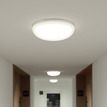 The modern hallway features Knox LED 13In Energy Star Flush Mount ceiling lights, with two more visible down the corridor. White walls and room number signs mounted by wooden door frames complete the look.