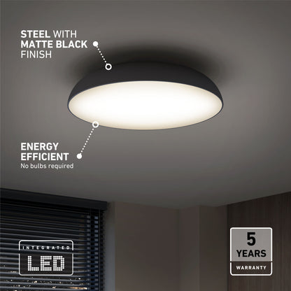 The Flint LED Flush Mount, featuring a matte black steel finish, shines in a room with partially visible window blinds. Text highlights its energy efficiency, integrated LED technology, and a 5-year warranty.