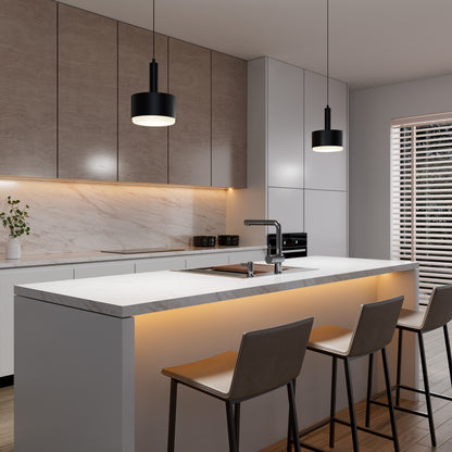 Modern kitchen features a marble island with three bar stools, wood cabinets, under-cabinet lighting, and the sleek Fritz Mini LED Pendant. A vase with greenery sits on the counter near the window with horizontal blinds and sink.