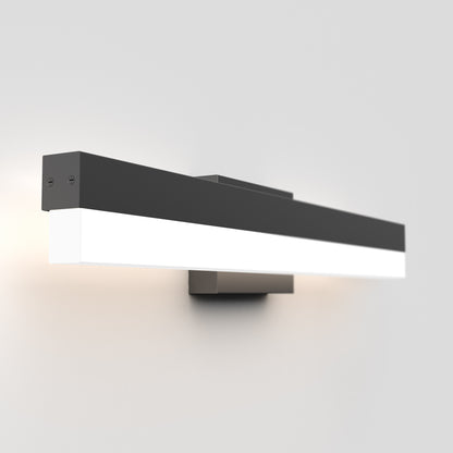 The Mystic LED Vanity Light is a modern wall-mounted fixture with a sleek black and white rectangular design, casting a soft glow on a plain light gray wall.