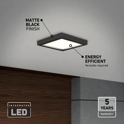 The Skylight Pro Square 7in 3K LED Flush Mount, in matte black, is installed above a sleek space with wood and gray walls. Energy efficient with integrated LEDs and a 5-year warranty—no bulb replacements needed.