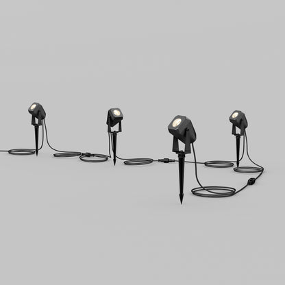 The Verner Plug-in Landscape Single CCT LED 4-pack features four weather-resistant pathway lights with stakes, linked by black cables and shown illuminated in a row on a plain light gray background for bright landscape lighting.