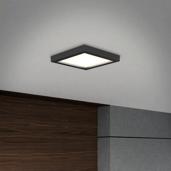 The Skylight Pro Square 7in 3K LED Flush Mount with a black frame is installed on a white ceiling above a wall featuring wood and gray textured paneling.