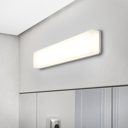 The Aster 27in Energy Star LED Vanity Light, a rectangular wall-mounted fixture, is installed above a large mirror in a modern bathroom with light gray walls and cabinetry.