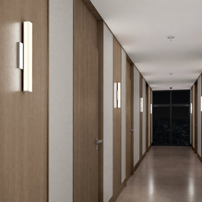 A modern hallway with wooden doors and light panels is illuminated by Mylo LED Vanity Light 16IN. A large window at the end displays a nighttime city view, and the polished floor reflects the stylish lighting.