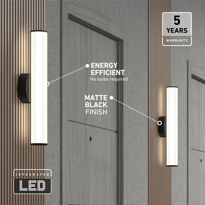 Two Kalio Indoor LED Wall Sconce 18" fixtures in matte black with integrated LEDs and a modern tubular design are mounted on a wood-paneled wall beside gray doors; energy efficiency and a 5-year warranty are featured.