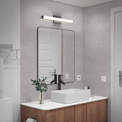 Modern bathroom with gray tiled walls, a rectangular mirror above a white sink with black faucet, wooden vanity, small plant, and the Mylo LED Vanity Light 24IN mounted above the mirror.