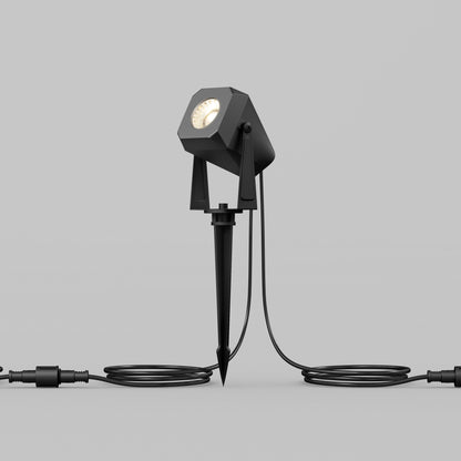 The Verner - Plug-in Landscape Single CCT LED 4-pack features a modern black spotlight with a stake base and coiled side cables, ideal for lasting outdoor landscape lighting with weather-resistant design. Shown upright against a plain gray background.