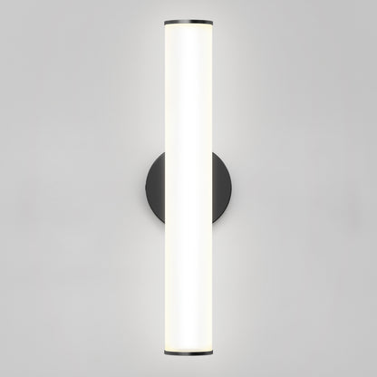 The Kalio Indoor LED Wall Sconce 18" features a vertical, cylindrical LED fixture that emits bright white light, mounted on a matte black base against a plain light gray wall. Suitable for 0-10V dimming and 120-277V applications.