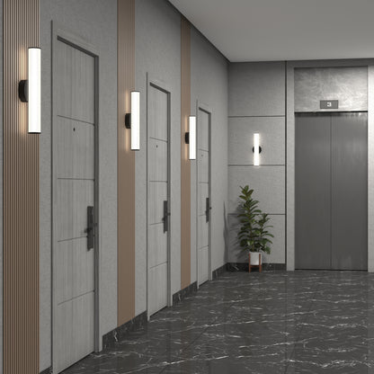 A modern hallway features four light wooden doors on the left, Kalio Indoor LED Wall Sconce 18" 0-10V 120-277V fixtures between them, a grey elevator on the right, marble flooring, and a potted plant beside the elevator.