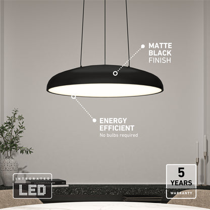 The Flint LED Pendant, with a matte black finish and integrated LED design, hangs above a table in a minimal room. Energy efficient and backed by a 5-year warranty. Candles and plants accent the background.