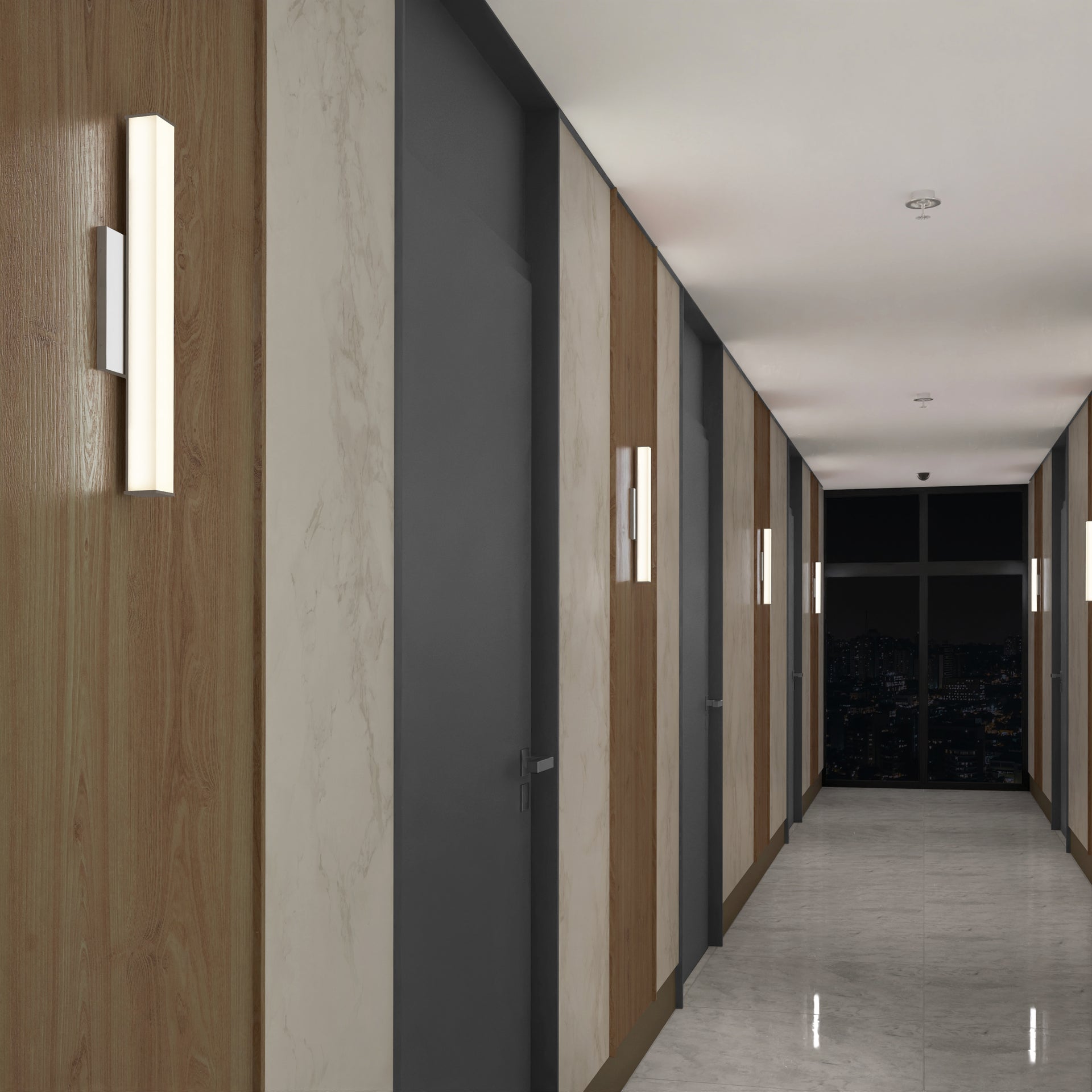 A modern hallway features light wood and marble wall panels, gray doors, shiny marble floors, and Mylo LED Vanity Light 16IN fixtures. Windows at the end display a night cityscape.