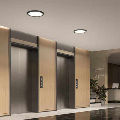 Three modern elevators with wood paneling and metal doors are set in a marble-floored lobby, where the reception desk, plants, and signs are brightly lit by 15" LED Skylights with three colour trim rings.