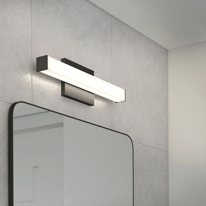 The Mylo LED Vanity Light 16IN with a black base is mounted above a frameless rectangular bathroom mirror on a gray tiled wall.