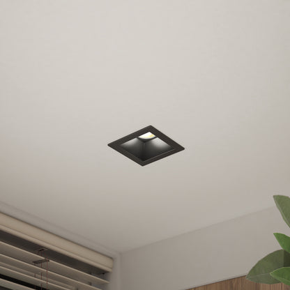 The Skyview 4in Regressed Square, 5CCT LED pot light with a black frame is installed in the white ceiling above a window with blinds and a green plant, offering adjustable colour-balance for versatile indoor or outdoor lighting.