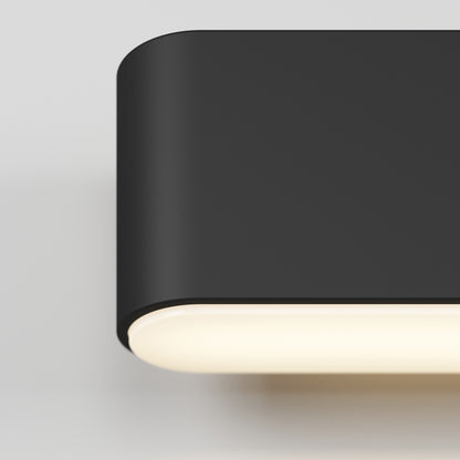 Close-up of the Willow LED Vanity 3CCT Light, a modern black wall sconce with rounded edges, mounted on a white wall and emitting a soft, warm glow from the bottom.