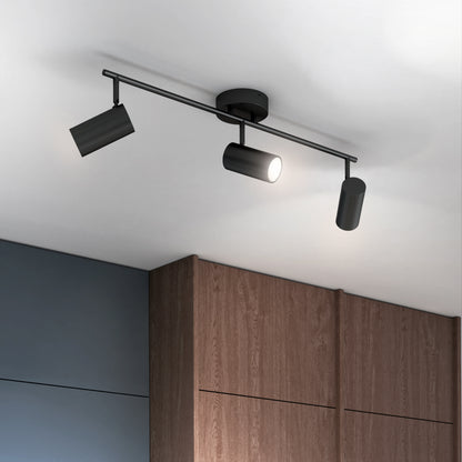 The Alpha LED Track 3-Light is a modern black ceiling fixture with three adjustable cylindrical spotlights, shown mounted above dark wood cabinets and gray walls, with one spotlight illuminated.