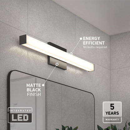 The Mylo LED Vanity Light 24IN, featuring a matte black finish, is mounted above a bathroom mirror on a gray tiled wall. Energy efficient and bulb-free, it includes a 5-year warranty.