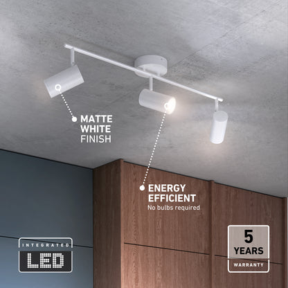 The Alpha LED Track 3-Light is a modern, matte white fixture with three adjustable heads, mounted on a concrete ceiling above wooden cabinets. It features energy efficiency, an integrated LED (no bulbs needed), and a 5-year warranty.