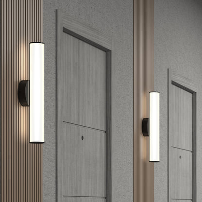 Kalio Indoor LED Wall Sconce 18" fixtures with cylindrical frosted glass shades are mounted beside light wood doors in a hallway with textured and vertical slat wall panels for a sleek, contemporary look.