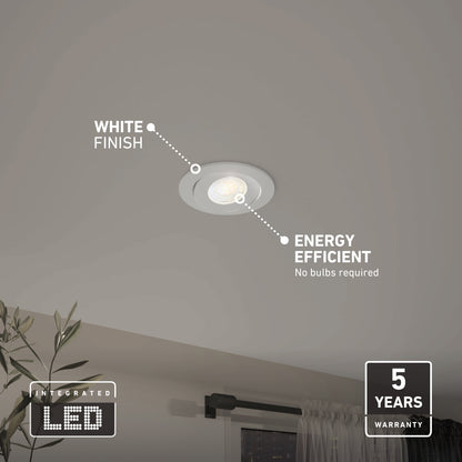 A Skyview 4in Gimbal Round, 5CCT LED is installed on a gray ceiling above a window. Text highlights its white finish, energy efficiency, JA8‑2022 compliance, and 5-year warranty. A potted plant sits below.