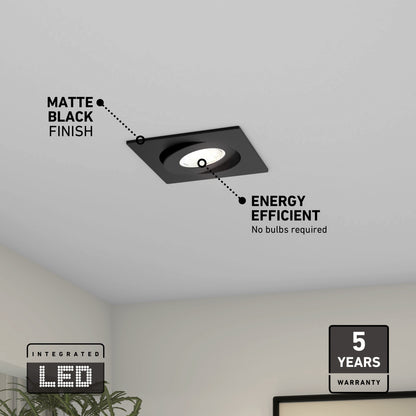 The Skyview 4in Gimbal Square, 5CCT LED is a matte black, recessed ceiling light with integrated LEDs, energy-efficient design (no bulbs needed), and a 5-year warranty. Below it, you can see a room corner and part of a plant.