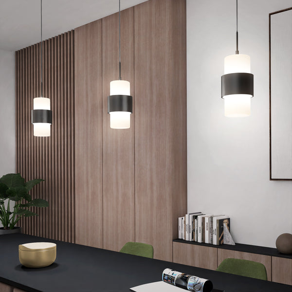 Modern interior featuring three Miko 3CCT LED Mini Pendant Black lights above a black countertop, with wood-paneled walls, a plant, books, a gold bowl, and partially visible artwork on a white wall in the background.