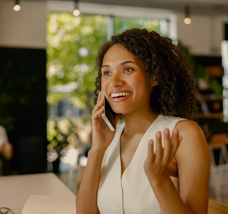 Woman talking on a phone in an indoor setting with blurred greenery in the background