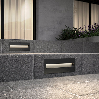 Modern outdoor steps feature Dark Sky Step Light Pro- Black 12in, with concrete planters and large windows with closed curtains behind. Purple flowers are visible near the top right corner.