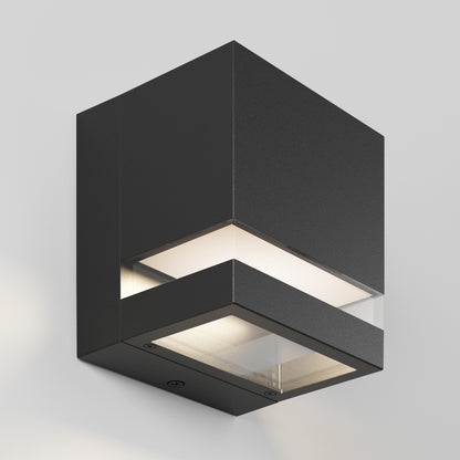 The Valor Square LED Indoor/Outdoor Wall Light is a modern black cube sconce with frosted glass panels on both illuminated sides, casting light up and down, and is mounted on a plain light gray wall.