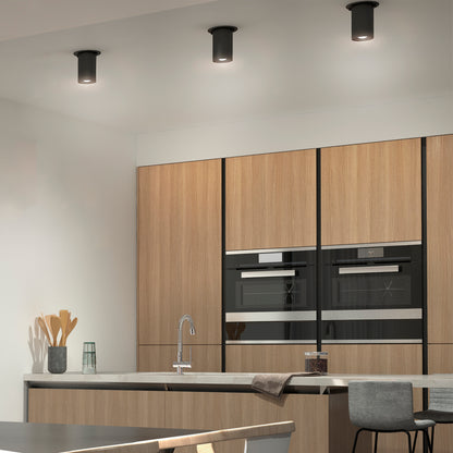 Modern kitchen with light wood cabinets, built-in black oven and microwave, a tall faucet sink, and a kitchen island with two gray stools. The space is illuminated by the Beam Pro 4 Integrated LED 2-IN-1 Ceiling Mount Pendant.