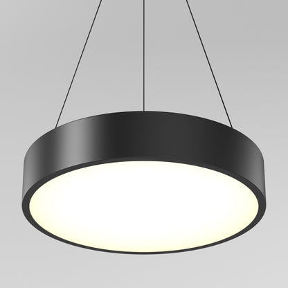 The Concerto LED Pendant, a sleek black circular light with a glowing white surface, hangs from the ceiling by three slim wires against a plain gray background.