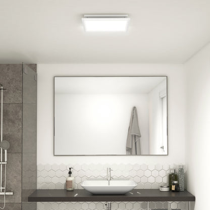 A modern bathroom features the 5 CCT Skylight Breeze Integrated LED Bathroom Fan, a large mirror above a white sink, hexagonal white tiles, a wall-mounted towel, and toiletries on the counter.