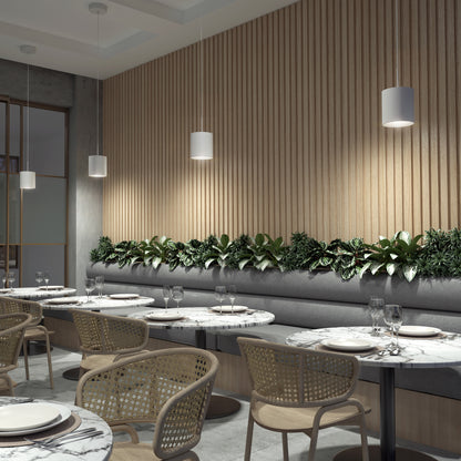 A modern restaurant with marble tables, wicker chairs, and gray built-in seating. Green plants line the backrest, while Beam Pro 8 Integrated LED 2-IN-1 Ceiling Mount Pendants hang above the seating area.
