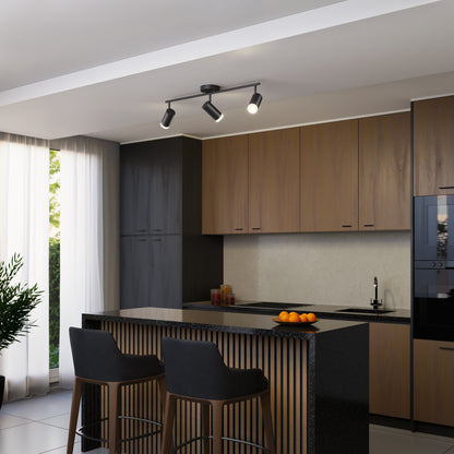 Modern kitchen with wood cabinets, black countertops, and a kitchen island with two black barstools. A bowl of oranges rests on the island. The ceiling features the 32" Blake 3L tracklight and large windows provide natural light.