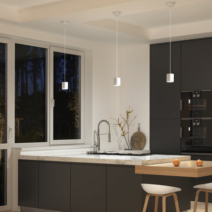 Modern kitchen with dark cabinets, marble countertops, and built-in appliances. Three Beam Pro 4 Integrated LED 2-IN-1 Ceiling Mount Pendants hang above the counter, illuminating a wooden breakfast bar with stools. Natural light streams through a window.