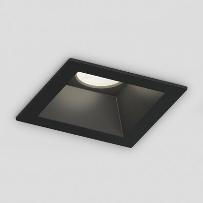 A Skyview 4in Regressed Square, 5CCT LED pot light fixture, black and IC-rated, with a single illuminated bulb, is recessed and mounted on a white ceiling.