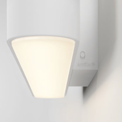 Close-up of the Willow LED Vanity 3CCT Light softly glowing with a frosted shade. The word "artika" is visible on the side, making it an ideal adjustable bathroom mirror light mounted on a light-colored wall.