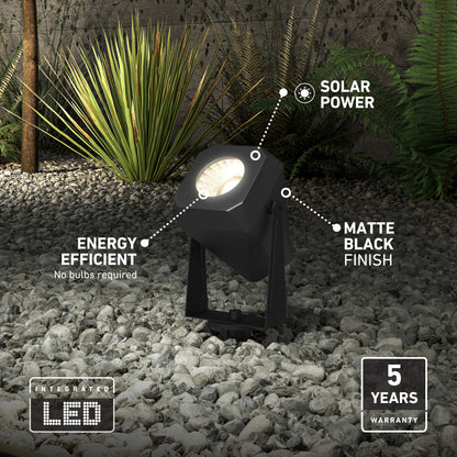 The Verner - Solar Landscape Single CCT LED 4-pack, shown in matte black on gray rocks by green plants, features energy-efficient integrated solar LEDs and includes a 5-year warranty.