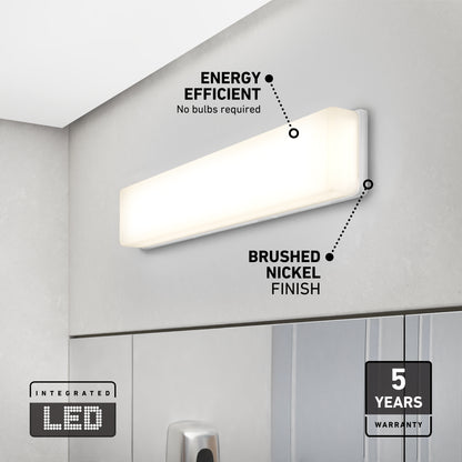 The Aster 27in Energy Star LED Vanity Light, featuring a brushed nickel finish, is mounted above a bathroom mirror. Labels showcase its energy efficiency, integrated LED technology, and a 5-year warranty.